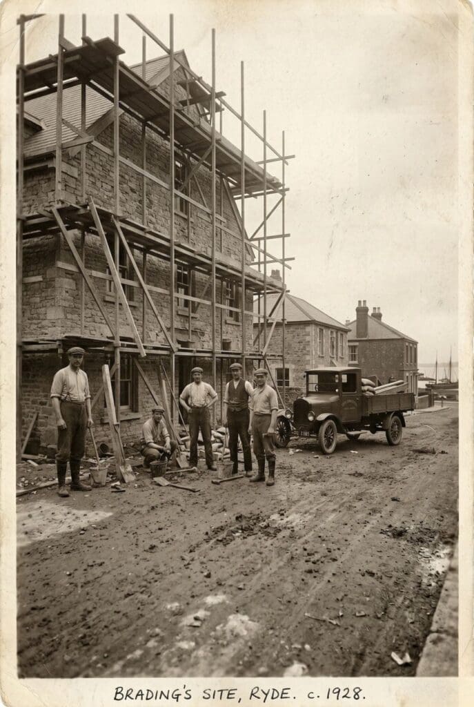 Vintage 1928 sepia photograph of Brading's construction site in Ryde, showing five workers standing in front of a stone building with wooden scaffolding and a classic truck.